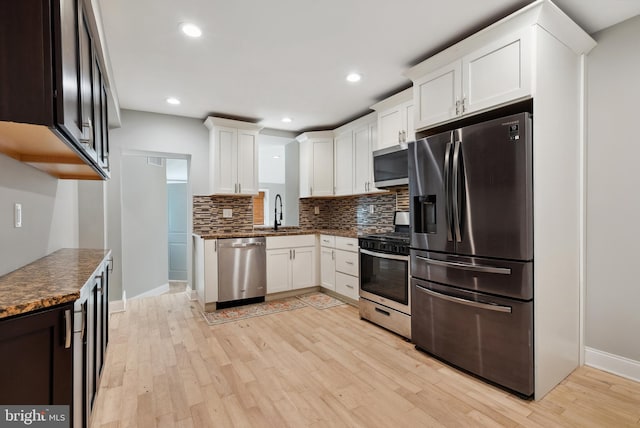 kitchen featuring light wood-style flooring, tasteful backsplash, appliances with stainless steel finishes, and a sink