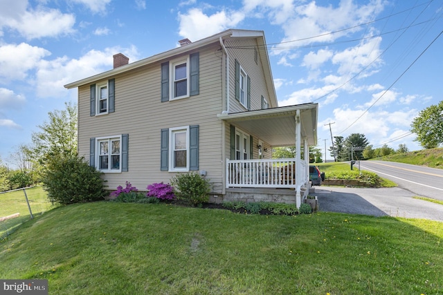 view of front facade with a front yard, covered porch, and a chimney