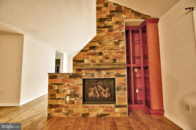 unfurnished living room with a textured ceiling, wood finished floors, lofted ceiling, and a fireplace