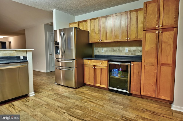 kitchen featuring beverage cooler, appliances with stainless steel finishes, decorative backsplash, and light wood-style flooring