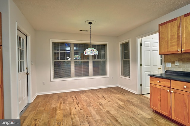 unfurnished dining area featuring light wood-type flooring, a textured ceiling, baseboards, and visible vents