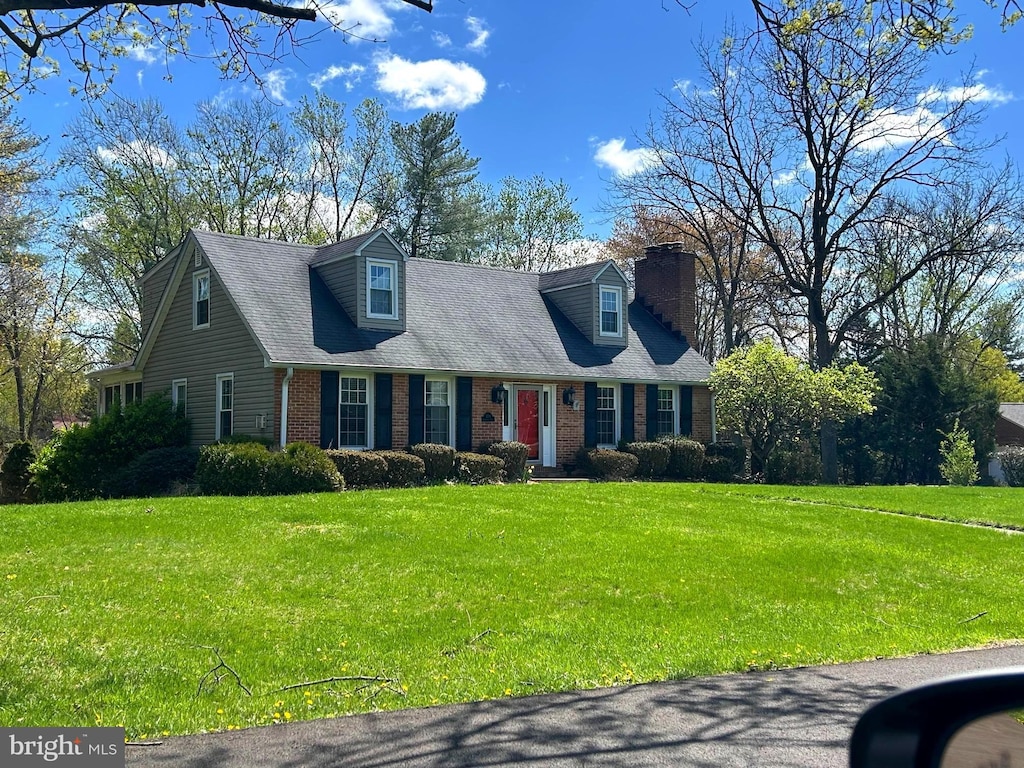cape cod home with brick siding, a chimney, and a front yard