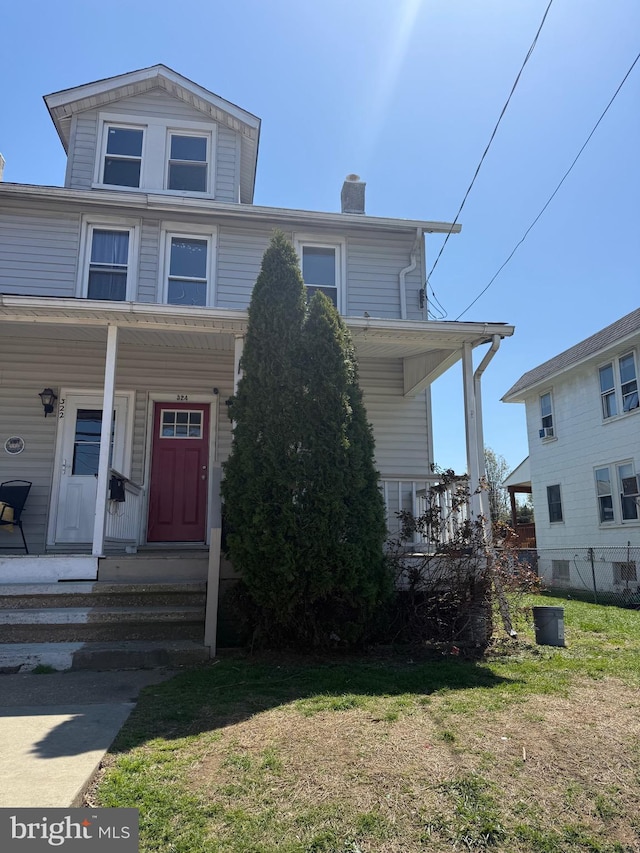 view of front of house featuring covered porch, a chimney, and a front yard