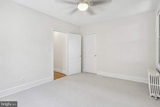 unfurnished bedroom featuring radiator heating unit, a ceiling fan, light colored carpet, and baseboards