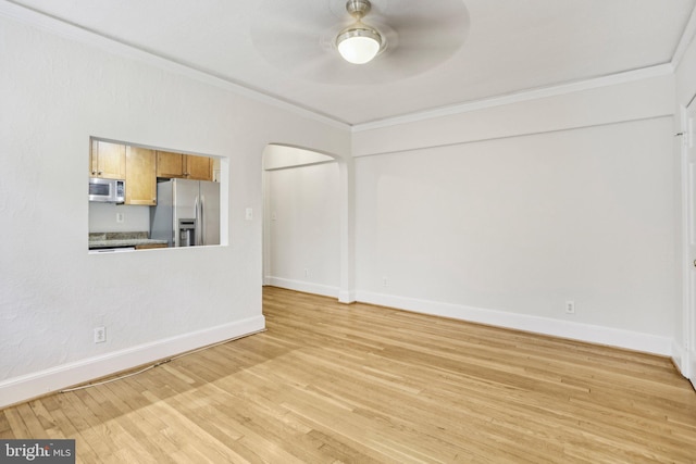 unfurnished living room with baseboards, arched walkways, ceiling fan, crown molding, and light wood-style flooring