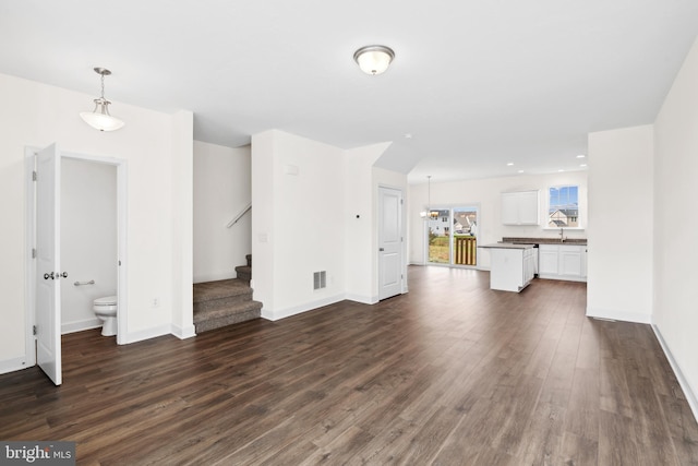 unfurnished living room with visible vents, baseboards, a sink, dark wood finished floors, and stairway