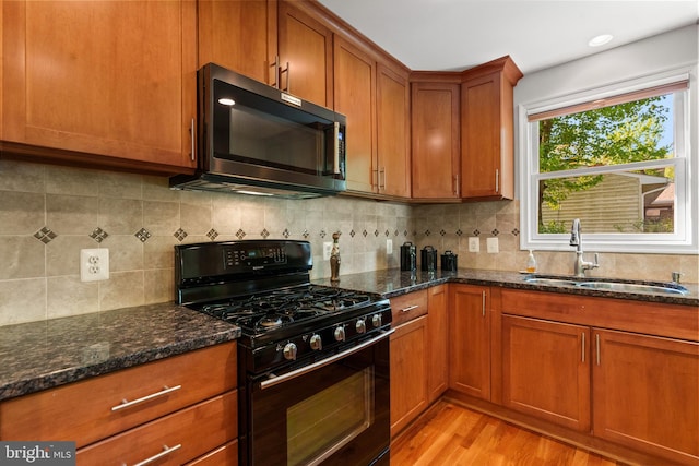kitchen featuring brown cabinetry, black gas stove, light wood-style flooring, a sink, and dark stone countertops