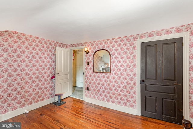 spare room with wallpapered walls, baseboards, and wood-type flooring