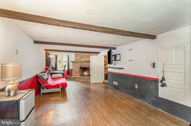 living area with hardwood / wood-style floors, a brick fireplace, beam ceiling, and wood walls