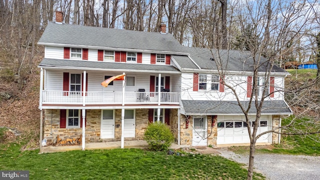 view of front of property with stone siding, driveway, a balcony, and a garage