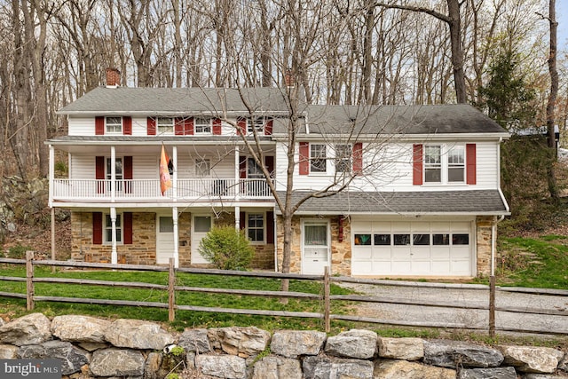 colonial-style house featuring dirt driveway, stone siding, a chimney, and a balcony