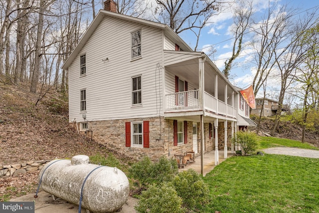 view of side of property with stone siding, a chimney, a balcony, and a yard