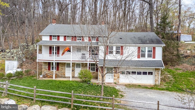 view of front of property featuring a front lawn, stone siding, covered porch, a garage, and gravel driveway