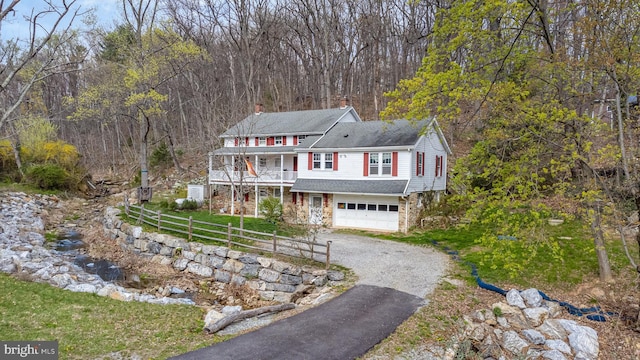 view of front of property featuring an attached garage, a chimney, aphalt driveway, and a wooded view