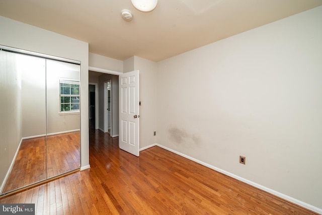 unfurnished bedroom featuring wood-type flooring, baseboards, and a closet