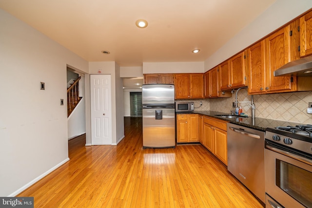 kitchen featuring appliances with stainless steel finishes, a sink, range hood, light wood-type flooring, and backsplash