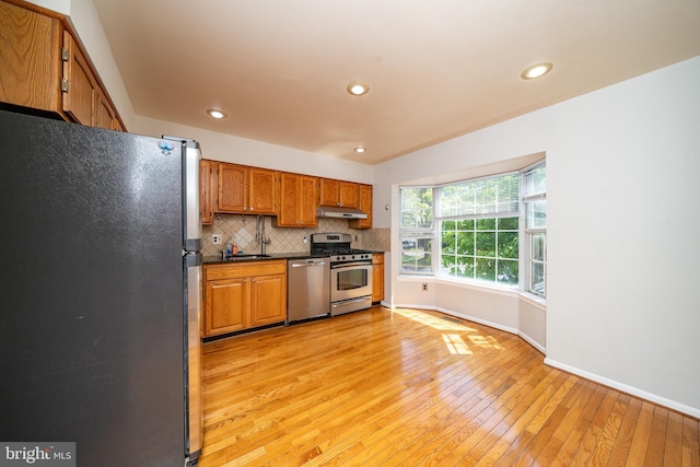 kitchen with dark countertops, appliances with stainless steel finishes, light wood-style floors, baseboards, and under cabinet range hood