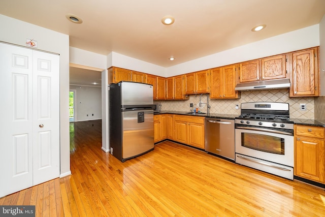kitchen featuring light wood-style flooring, backsplash, under cabinet range hood, and stainless steel appliances