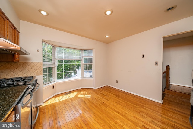 kitchen featuring stainless steel gas range oven, light wood-style floors, brown cabinetry, baseboards, and backsplash