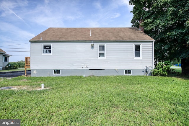 rear view of house featuring a shingled roof, a chimney, and a lawn
