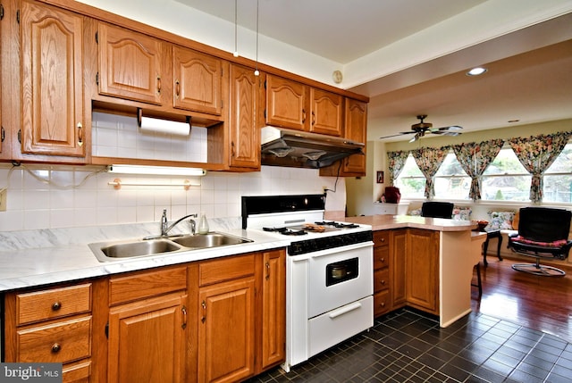 kitchen with a sink, light countertops, dark tile patterned flooring, under cabinet range hood, and white stove