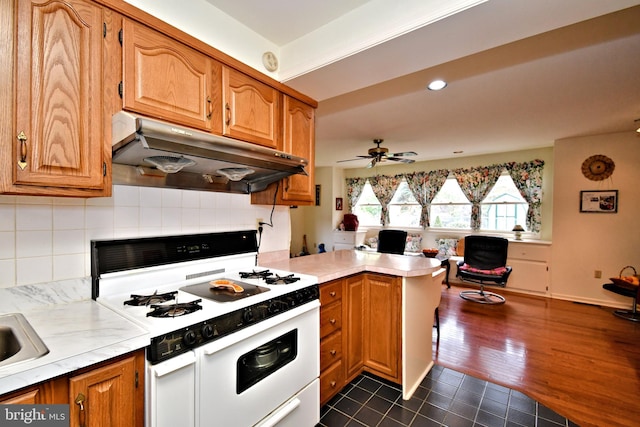 kitchen featuring light countertops, a peninsula, under cabinet range hood, and white gas stove