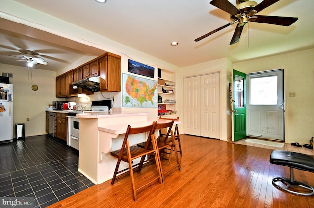 kitchen featuring a ceiling fan, a kitchen bar, light countertops, under cabinet range hood, and stainless steel appliances