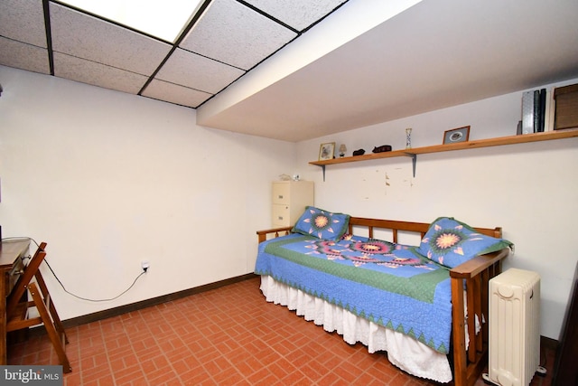 bedroom featuring radiator heating unit, baseboards, brick patterned floor, and a drop ceiling