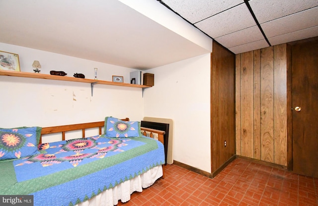 bedroom featuring baseboards, brick patterned floor, and wood walls