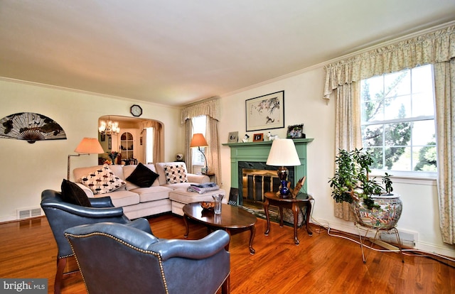 living area with visible vents, ornamental molding, wood finished floors, a high end fireplace, and arched walkways