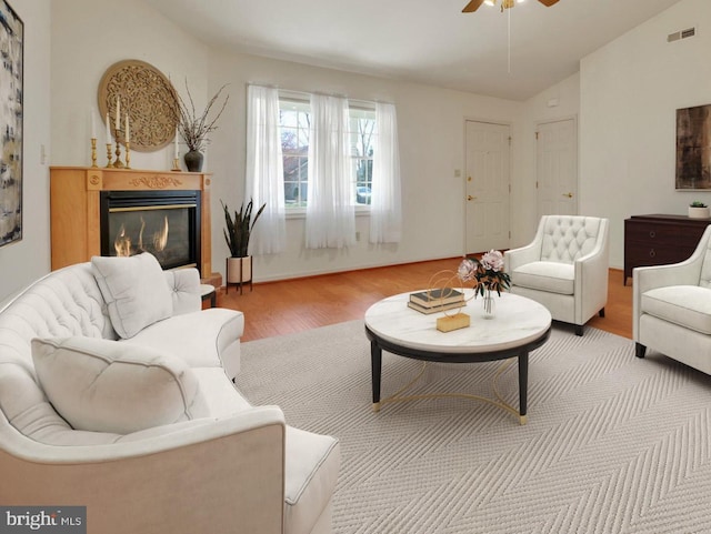 living room with ceiling fan, a glass covered fireplace, vaulted ceiling, visible vents, and wood finished floors