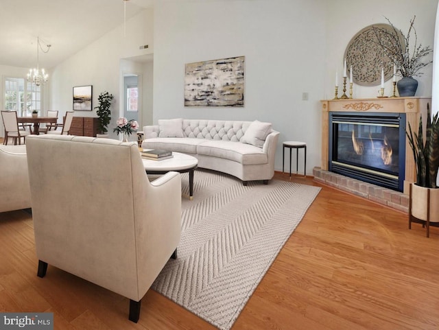 living room with an inviting chandelier, high vaulted ceiling, a glass covered fireplace, visible vents, and wood finished floors