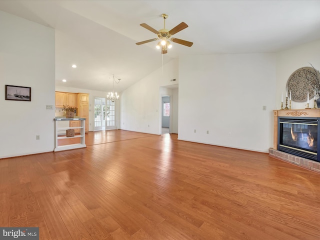 unfurnished living room featuring light wood-style floors, a brick fireplace, ceiling fan with notable chandelier, and lofted ceiling