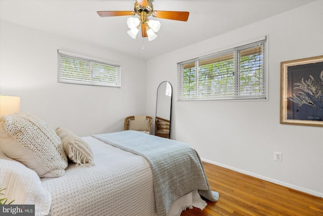 bedroom with baseboards, a ceiling fan, wood finished floors, and multiple windows