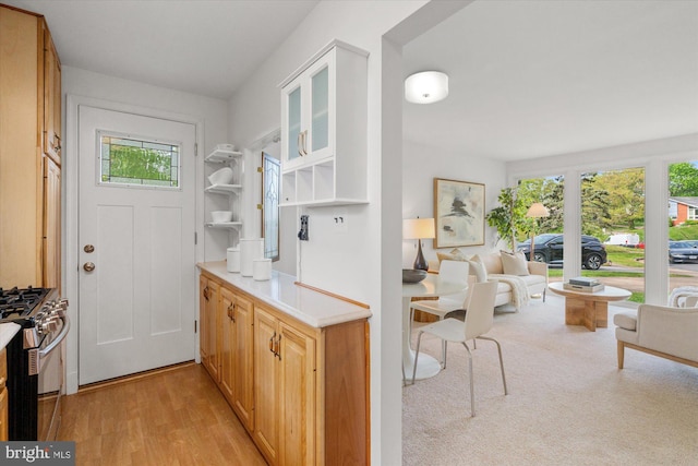 kitchen with light wood-style floors, stainless steel range with gas stovetop, light countertops, open floor plan, and glass insert cabinets