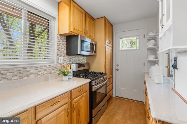 kitchen with open shelves, appliances with stainless steel finishes, light countertops, decorative backsplash, and light wood-type flooring