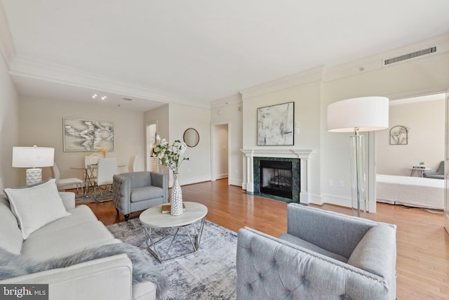 living room with visible vents, ornamental molding, wood finished floors, baseboards, and a high end fireplace