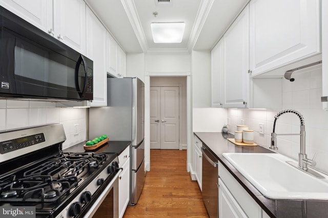 kitchen with a sink, light wood finished floors, stainless steel appliances, white cabinetry, and decorative backsplash
