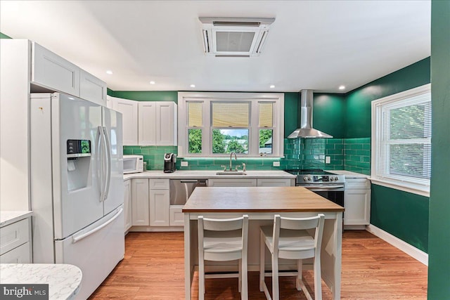 kitchen featuring tasteful backsplash, light wood-type flooring, wall chimney range hood, a sink, and stainless steel appliances