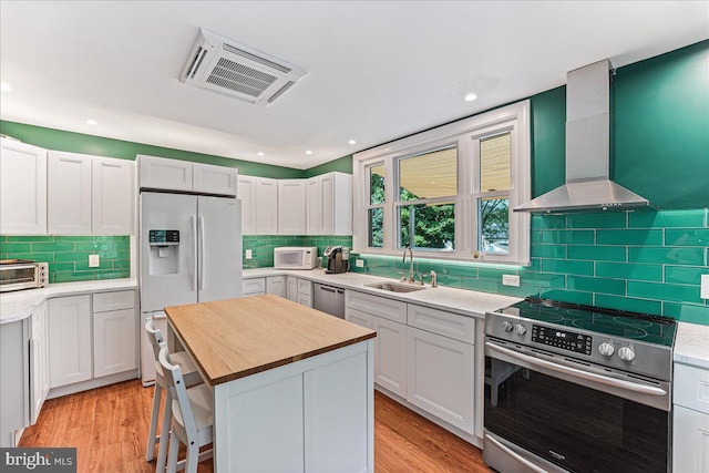 kitchen with visible vents, wall chimney exhaust hood, a sink, light wood-style floors, and stainless steel appliances