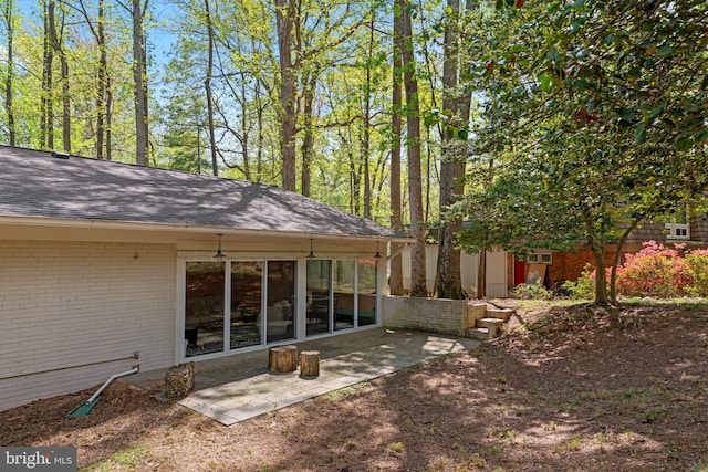 rear view of house featuring a shingled roof, brick siding, and a patio