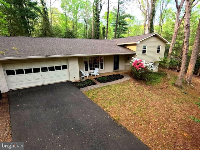 tri-level home featuring a shingled roof, driveway, a porch, brick siding, and a garage