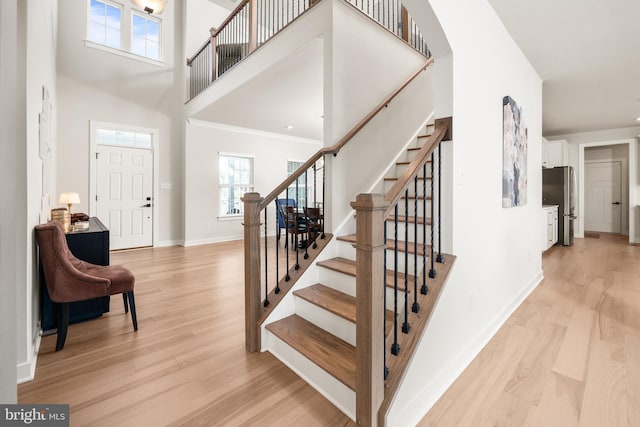 entrance foyer with light wood finished floors, a towering ceiling, stairs, and a healthy amount of sunlight