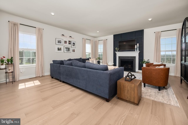 living room featuring recessed lighting, baseboards, a large fireplace, and light wood-style flooring