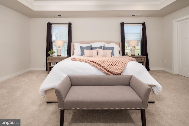 bedroom featuring visible vents, a tray ceiling, multiple windows, and light colored carpet