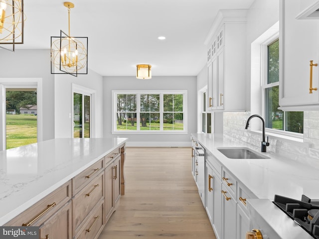 kitchen featuring tasteful backsplash, a sink, hanging light fixtures, light wood finished floors, and a notable chandelier