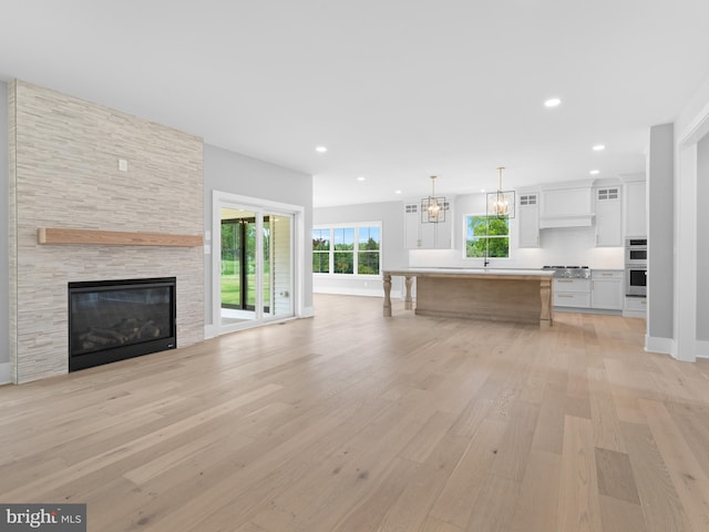 unfurnished living room with light wood-style flooring, a chandelier, a stone fireplace, and recessed lighting