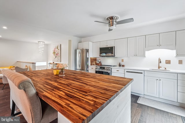 kitchen featuring white cabinets, a sink, ceiling fan, stainless steel appliances, and dark wood-type flooring
