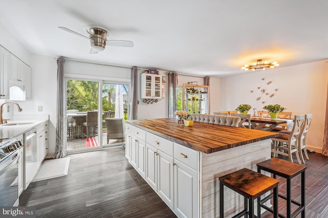 kitchen with a sink, wooden counters, a ceiling fan, a kitchen bar, and dark wood-type flooring