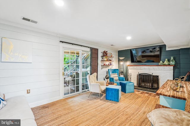 living area with wooden walls, a brick fireplace, visible vents, and crown molding